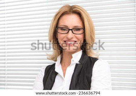 Laughing business woman in white shirt. Attractive mature businesswoman on white shutters smiling
