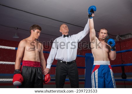 two boxer men standing in ring. referee lifting winner hand announcing victory