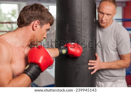 boxer and his coach doing some punching with bag. Boxer and his coach practicing some moves