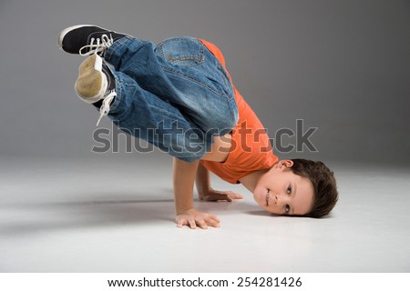 little break dancer showing his skills on grey background. Hip hop dancer boy performing isolated over dark background
