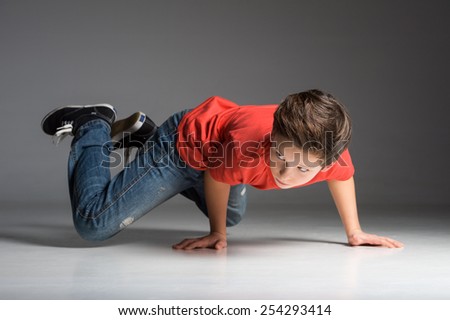 little break dancer showing his skills on grey background. Hip hop dancer boy performing isolated over dark background