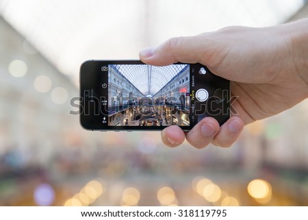 Russia, Moscow - July 25, 2015: The hand of young man who is taking the picture inside historical GUM department store with his smartphone on July 25, 2015 in Moscow, Russia.