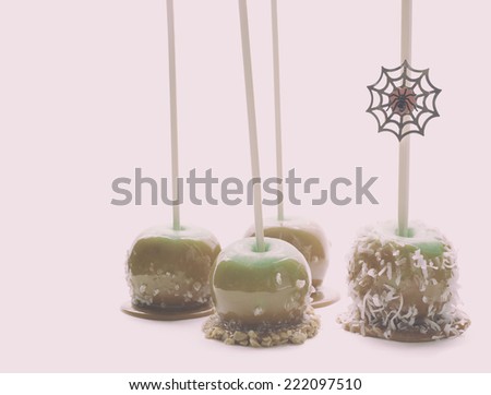 Four green caramel apples with sea salt, toffee and coconut sprinkles on parchment paper with a Halloween spider decoration.  Analog filter.