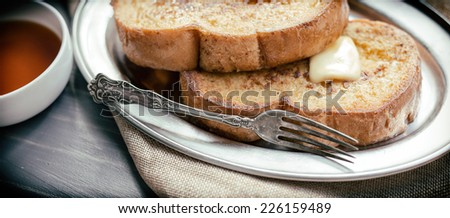 Two pieces of French toast with butter and a small ramekin of syrup.