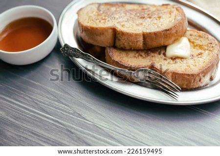 Two pieces of French toast with butter and a small ramekin of syrup.