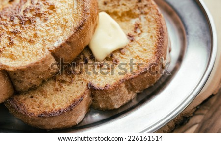 Two pieces of French toast with butter on a silver plate.