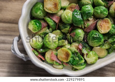 Fresh sauteed Brussels sprouts with ham in an ornate serving dish on a wooden table.