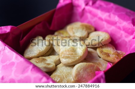 A gift box with hot pink tissue paper filled with heart shaped pastries for Valentine's day.