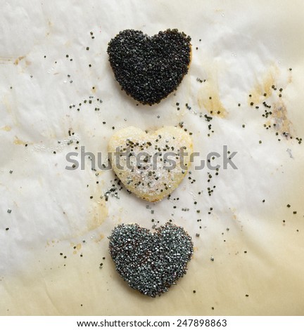 Three heart shaped sugar cookies decorated with various colors of coarse sugar sprinkles on parchment sheet.