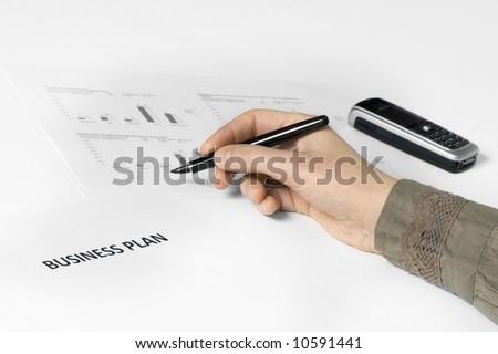 paper on desk with business plan on it. hand holding pen. paper with graphics on the background. cellphone on background.
