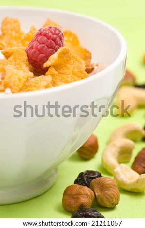 bowl of corn flakes cereal with raspberry, nuts and milk. Green background.