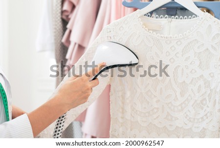 Using steaming iron to ironing dress in laundry room. Doing stream vapor iron for press clothes in hand. Showroom or atelier