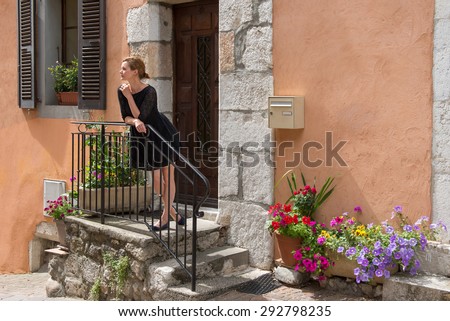Elegant woman stands on the porch of the house. Porch decorated with colorful flowers.