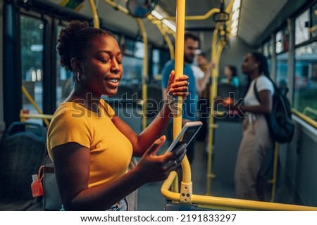An attractive african american woman using a smartphone while riding a bus in the night. Young beautiful black woman using public transportation. Illuminated by the city light. Foto stock © 