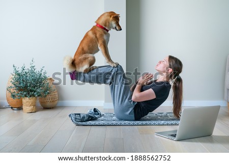 Doga or Doga yoga is the practice of yoga as exercise with dogs. Young woman in yoga position balancing with her dog. Home online training with a pet