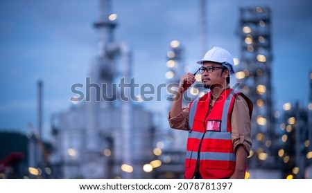 Engineer wearing safety uniform and helmet looking with radio communication conversation checking and inspection by oil refinery factory at night time background. Stockfoto © 