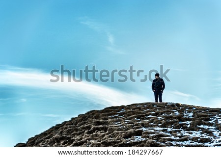 Man on a hill looking away thinking under the cloudy sky