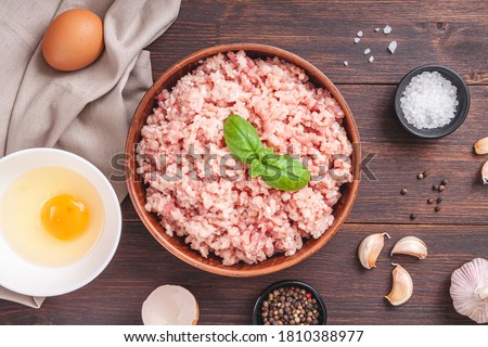 Raw minced meat in bowl on wooden table and ingredients. Ground meat with ingredients for cooking on dark background with copy space. Top view or flat lay