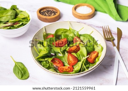 Summer green salad in white bowl plate on grey table. Healthy salat from tomato, spinach, onion and green leaves with oil for dinner or lunch. Vegetarian food concept. Top view on gray stone backgroun Imagine de stoc © 