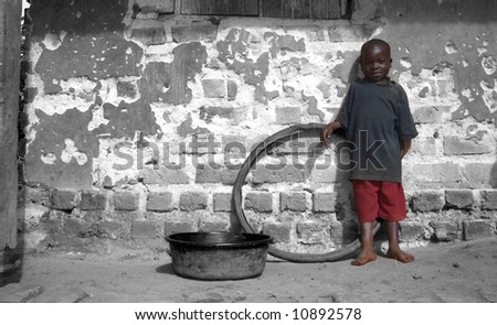 A poor african boy standing in front of his house.