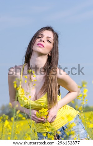 Yellow blooming field, cute fit young lady in yellow shirt. Nice decollete and serious look