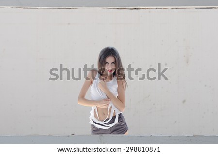 Slim female standing behind of a cement window wearing torn shirt, straight hair and bolt red lips