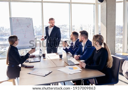 The boss stands near the board with graphs, demonstrates statistics, various personnel attending the training, introduces the new products of the company, reports on the results of work for partners.