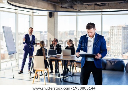Successful handsome male mentor, director, businessman in a suit at the office. Working day concept. Team meeting with the boss in the foreground