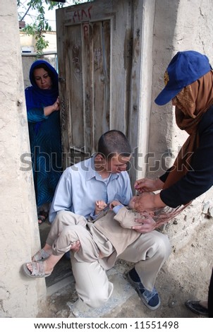 Afghan volunteer polio vaccinator vaccinates boy