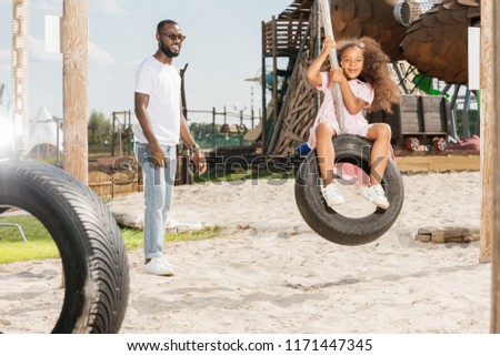 african american father standing near smiling daughter on tire swing at amusement park Imagine de stoc © 