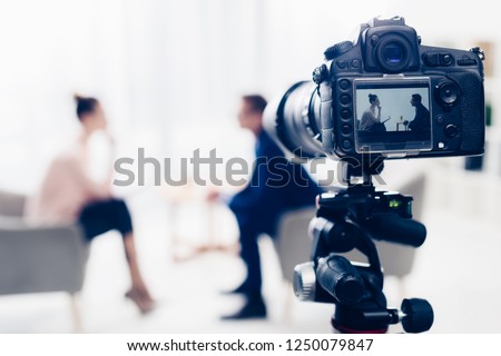 businessman giving interview to journalist in office, camera on tripod on foreground Foto stock © 