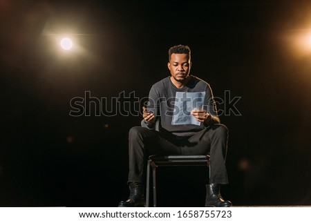 handsome african american actor holding scenario on stage during rehearse