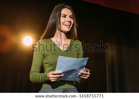 cheerful actress performing role with screenplay on stage in theatre