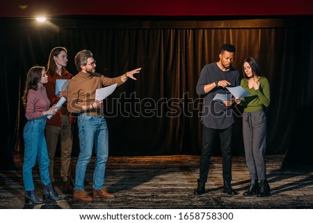 young multiethnic actors and actresses rehearsing with mature theater director on stage