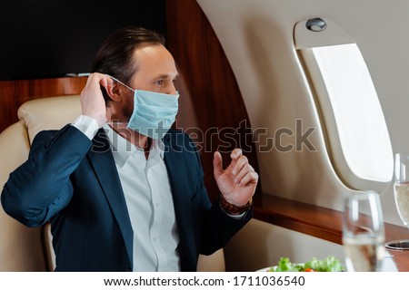 Selective focus of businessman putting on medical mask near champagne and salad on table in airplane Stock foto © 