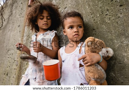 Selective focus of poor african american boy holding dirty teddy bear while begging alms near sister on urban street ストックフォト © 