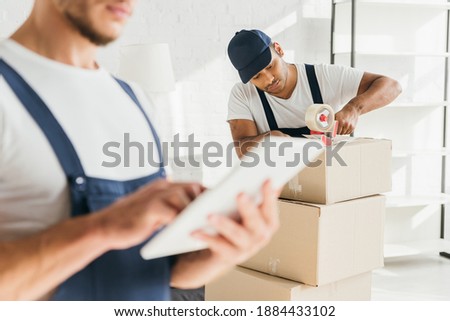 indian mover packing box near coworker holding digital tablet on blurred foreground  Stockfoto © 