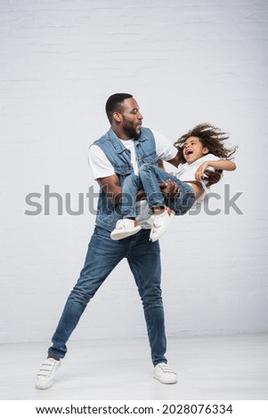 happy african american man playing with thrilled daughter while holding her in hands on grey ストックフォト © 