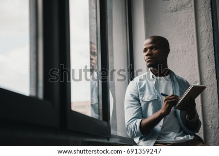 Portrait of young handsome african american man looking at window and writing notes Stock foto © 