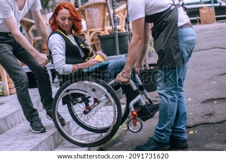 Waiters lift a girl in a wheelchair up the steps without a ramp. A woman is going to have lunch in a cafe inaccessible to people with special needs. Selective focus Foto d'archivio © 