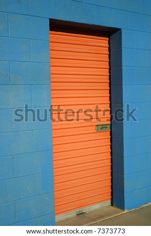 Bright orange door to storage unit in bright blue building