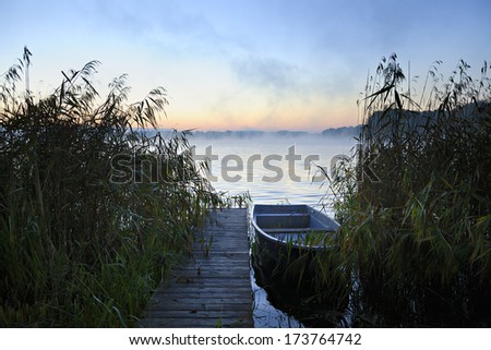Small Wooden Dock with Fishing Boat on Lake at Sunrise, Mist Rising from Water