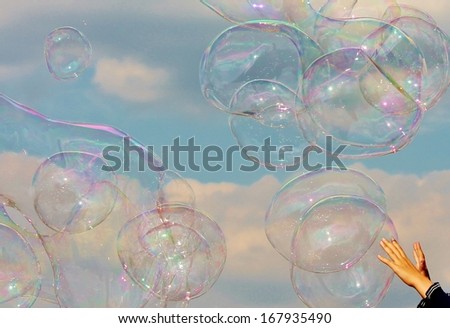 Hands reach for Soap Bubbles floating on the breeze in the blue and cloudy sky