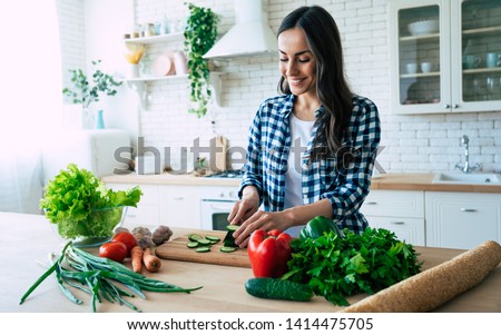 Beautiful young woman is preparing vegetable salad in the kitchen. Healthy Food. Vegan Salad. Diet. Dieting Concept. Healthy Lifestyle. Cooking At Home. Prepare Food. Cutting ingredients on table Foto stock © 
