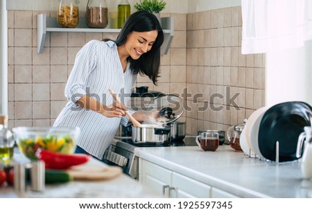 Beautiful happy young woman is cooking in the home kitchen and testing some soup from the pan on the stove Foto stock © 