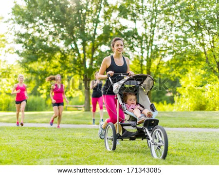 Woman pushing her little girl in a toddler while running outside with friends