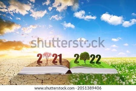 Open book with number 2021 and 2022. Dry country with cracked soil and spring meadow in sunny day. Concept of Happy New Year. Global warming or climate change theme.