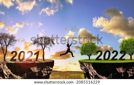Girl jumping from arid land with number 2021 on lush landscape with number 2022. Concept of Happy New Year. Global warming or change climate theme.