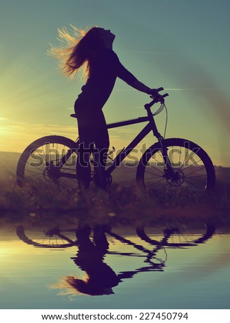Girl on a bicycle in the sunset reflected on the water surface