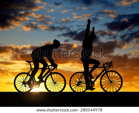silhouette of two cyclists riding a road bike at sunset